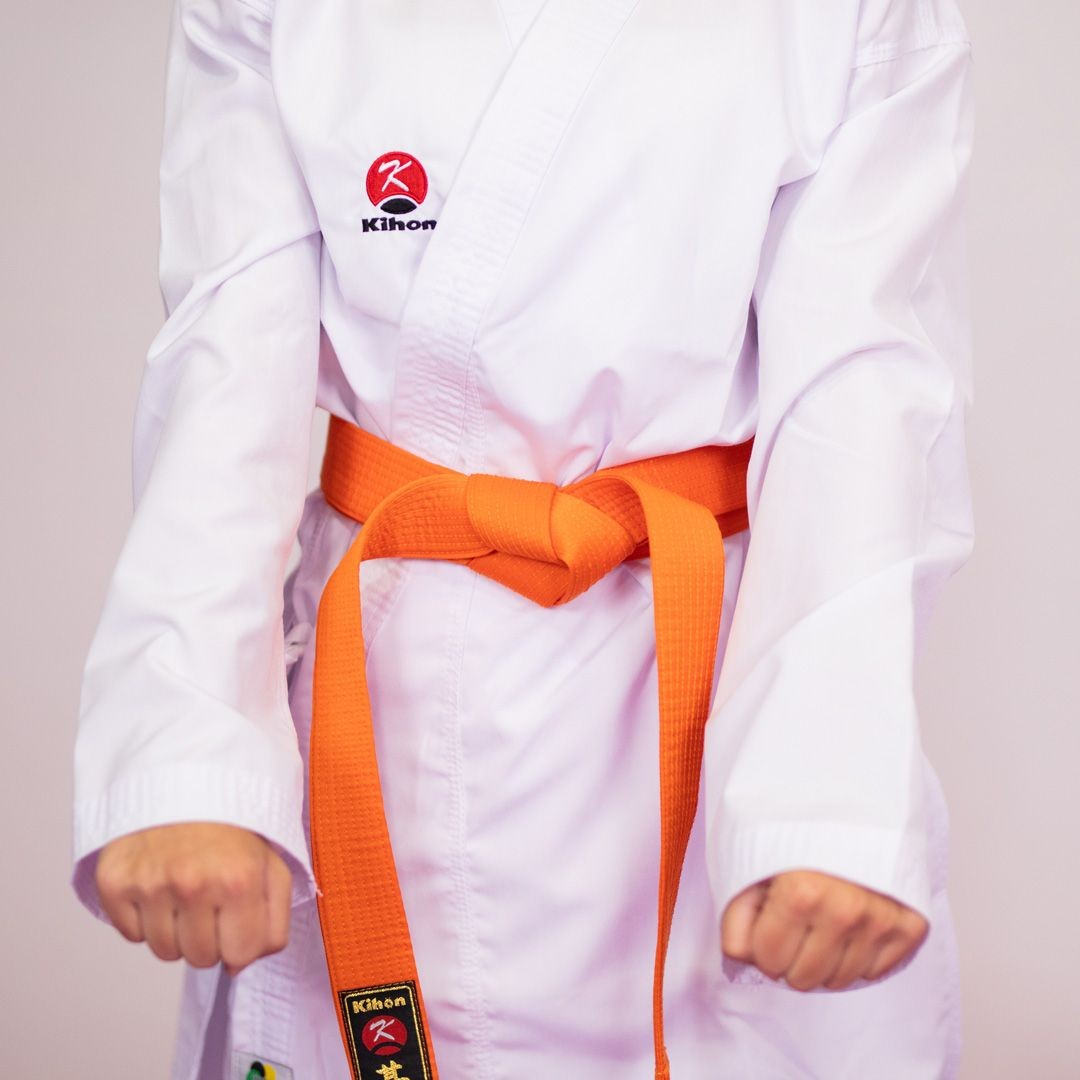 Person wearing a karate gi with an orange belt, displaying fists in a ready stance.