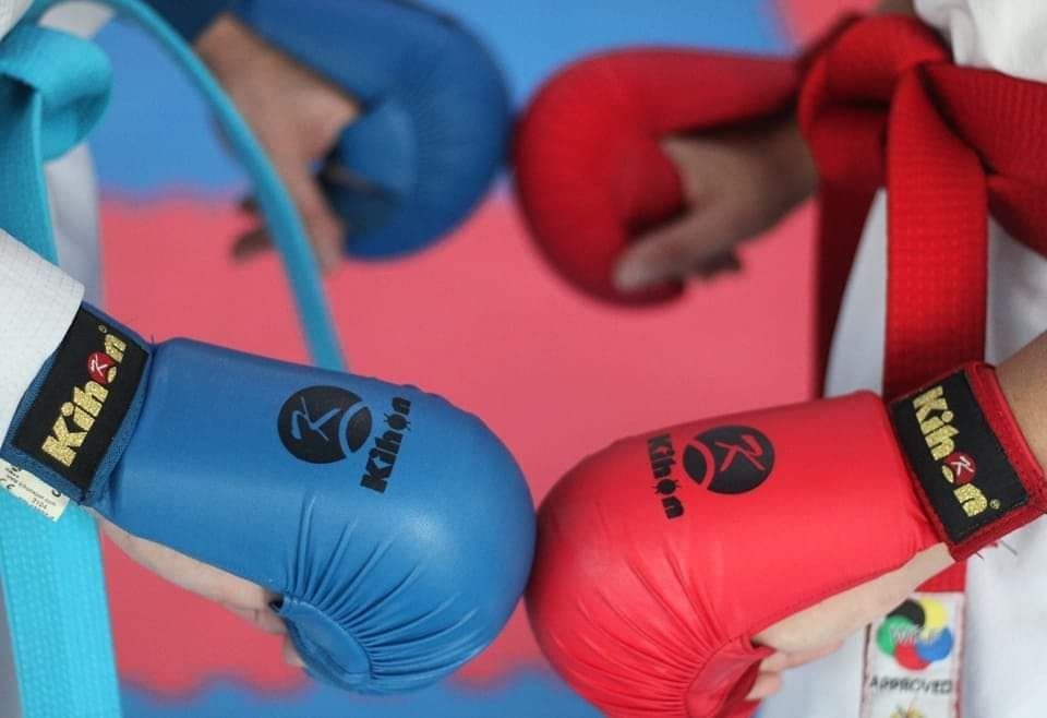 Close-up of red and blue boxing gloves in a fist bump, with martial arts belts visible.